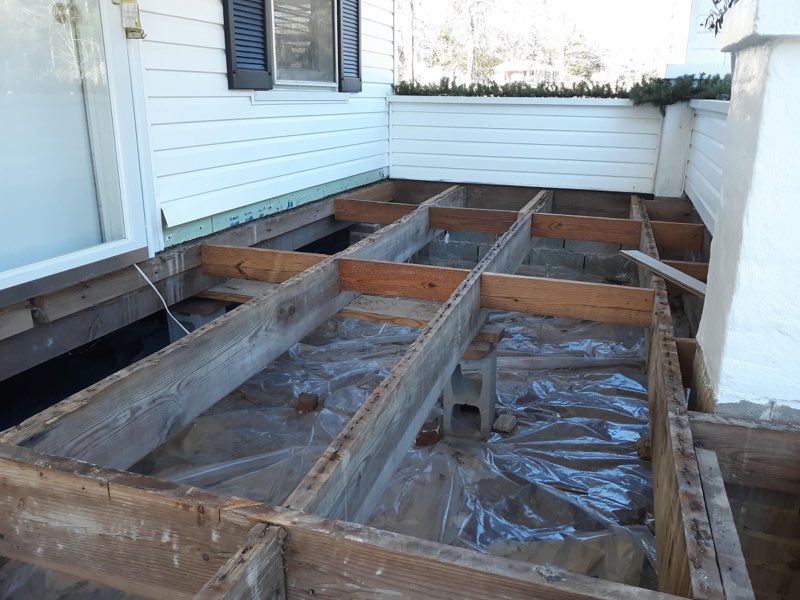 Deck framing and floor joists under construction beside a house