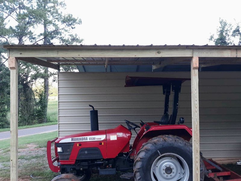 Post-frame carport sheltering a red Mahindra tractor